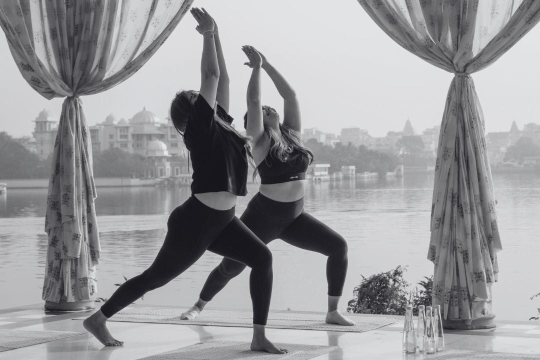 Two people practicing yoga next to water