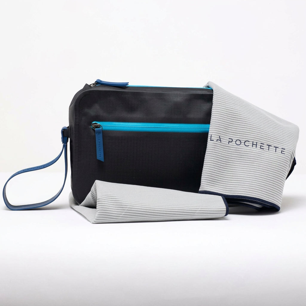 A black La Pochette Waterproof Aqua Bag with bright blue detachable handle and zips shown with a Gray La Pochette microfiber towel with blue edging.  On a white background 