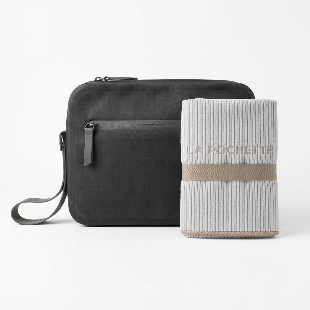 A black waterproof La Pochette  Aqua Bag, shown with a grey microfiber towel with taupe edging and La Pochette embroidered into it in taupe 
On a white background