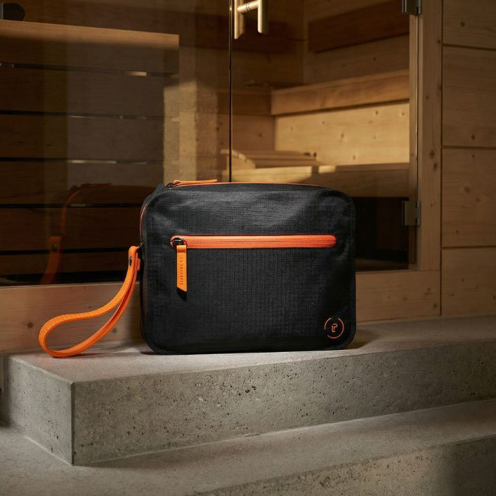 Black waterproof Aqua Bag with bright orange trims on a ledge outside a sauna