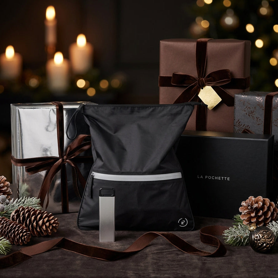 A Black La Pochette antibmicrobial Sweat Bag with silver zip. a silver supplement box is in front of it. They are surrounded by gifts with brown and silver wrapping and bows.
