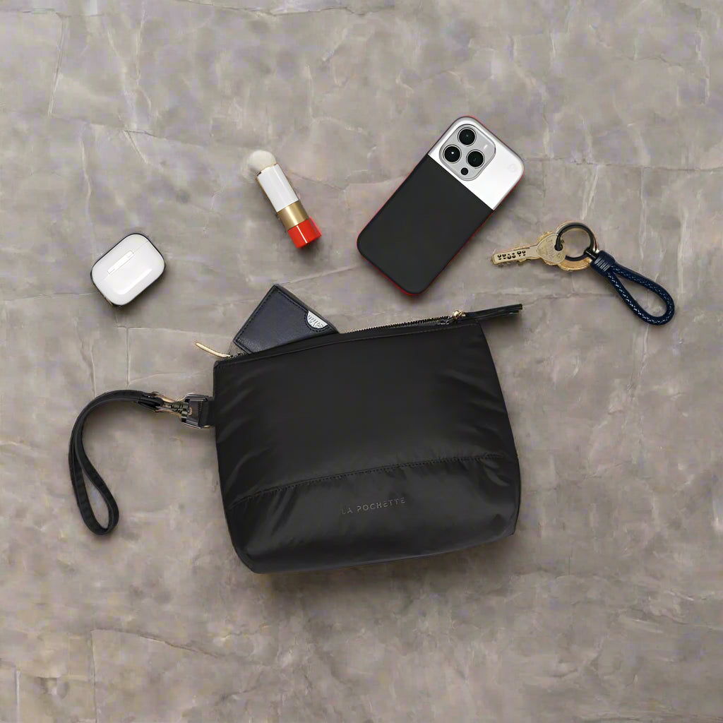 Black pouch with phone, keys, and other items on a marble background