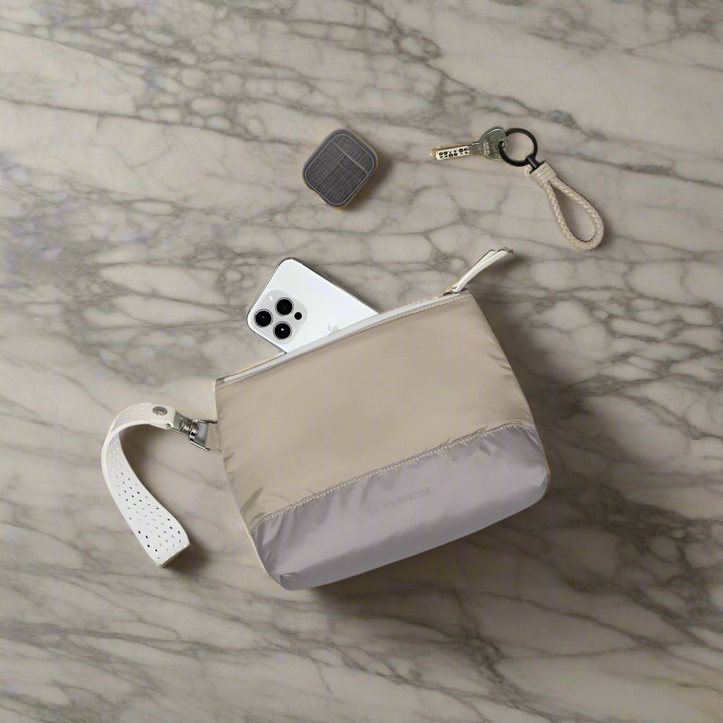 Beige and gray clutch bag with phone, key, and AirPods on a marble surface