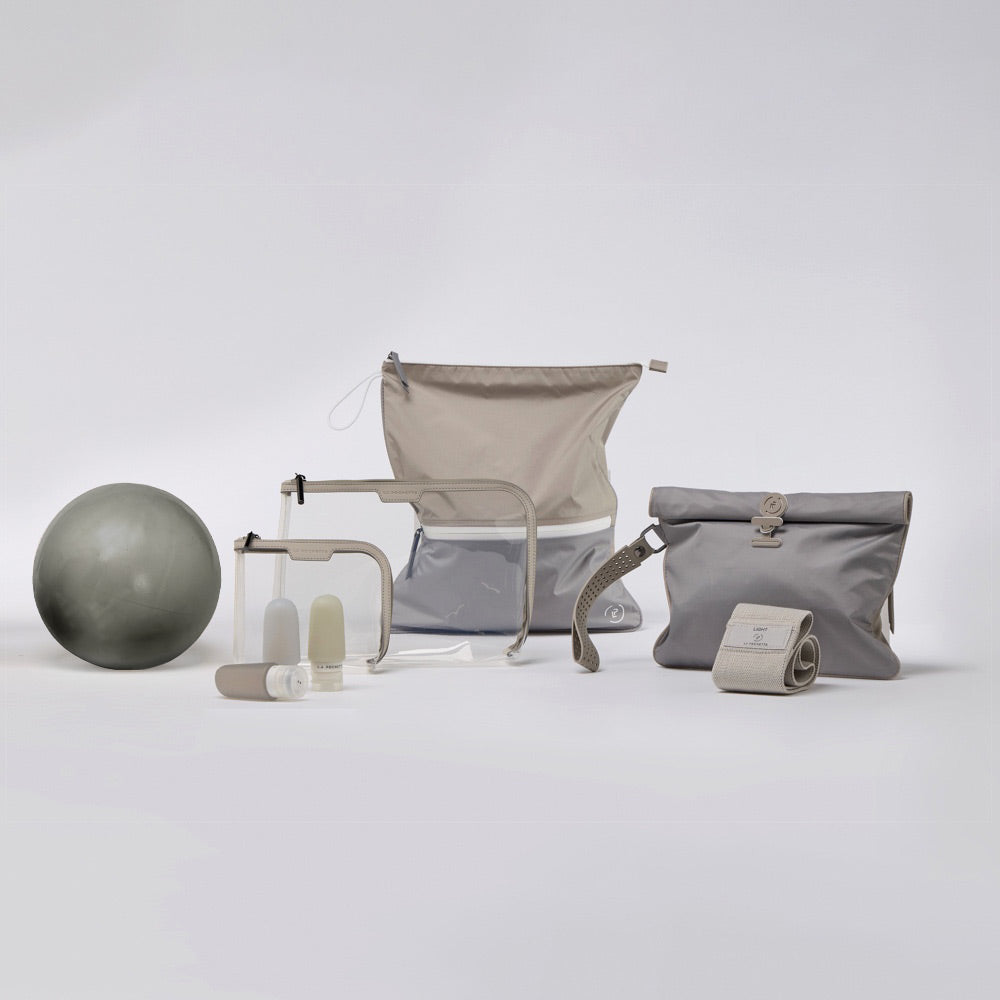 gift set for the woman who loves wellness including a la pochette sweat bag, wet bag, resistance band, inflatable pilates ball, small and large clear pouch, and silicone travel bottles. All in grey and beige tonal colours 