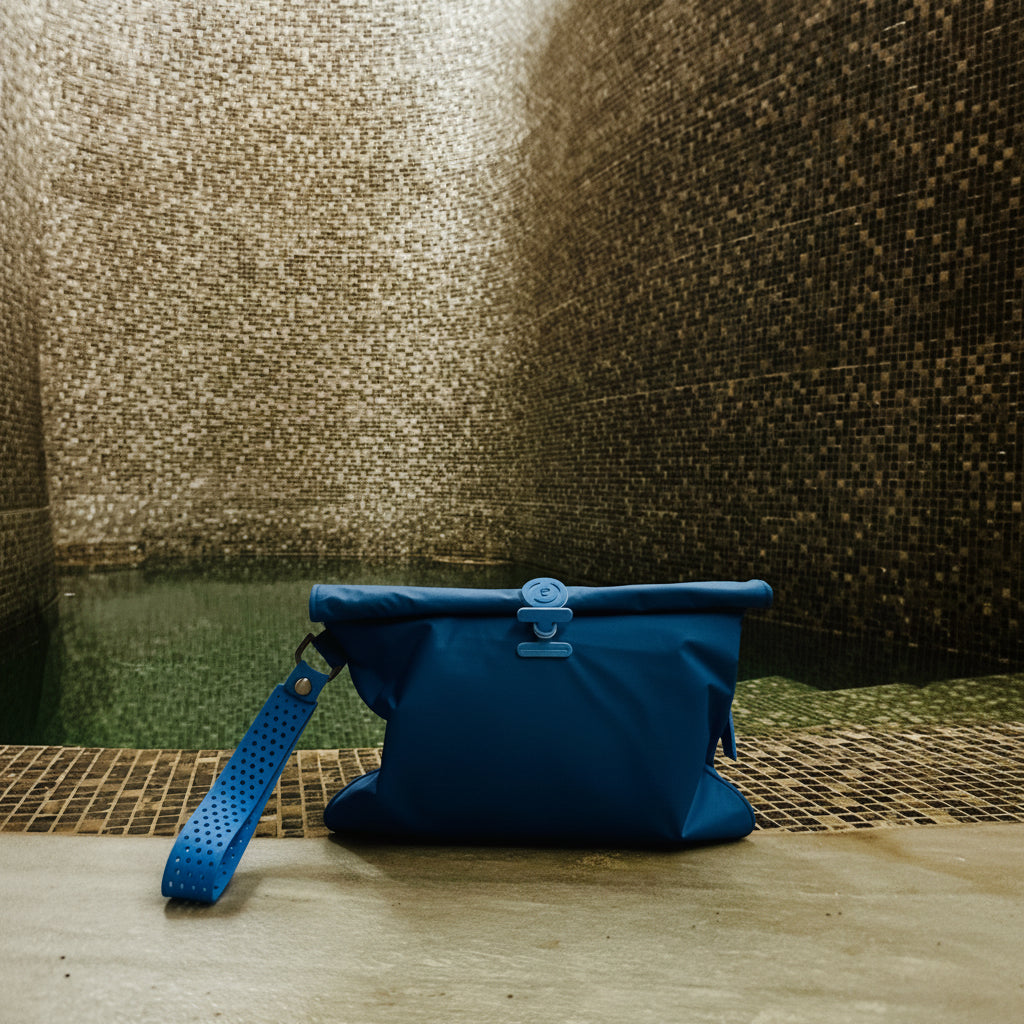 A blue waterproof La Pochette wet bag with a matching blue wristlet strap, infant on cold plunge pool on tiled floor