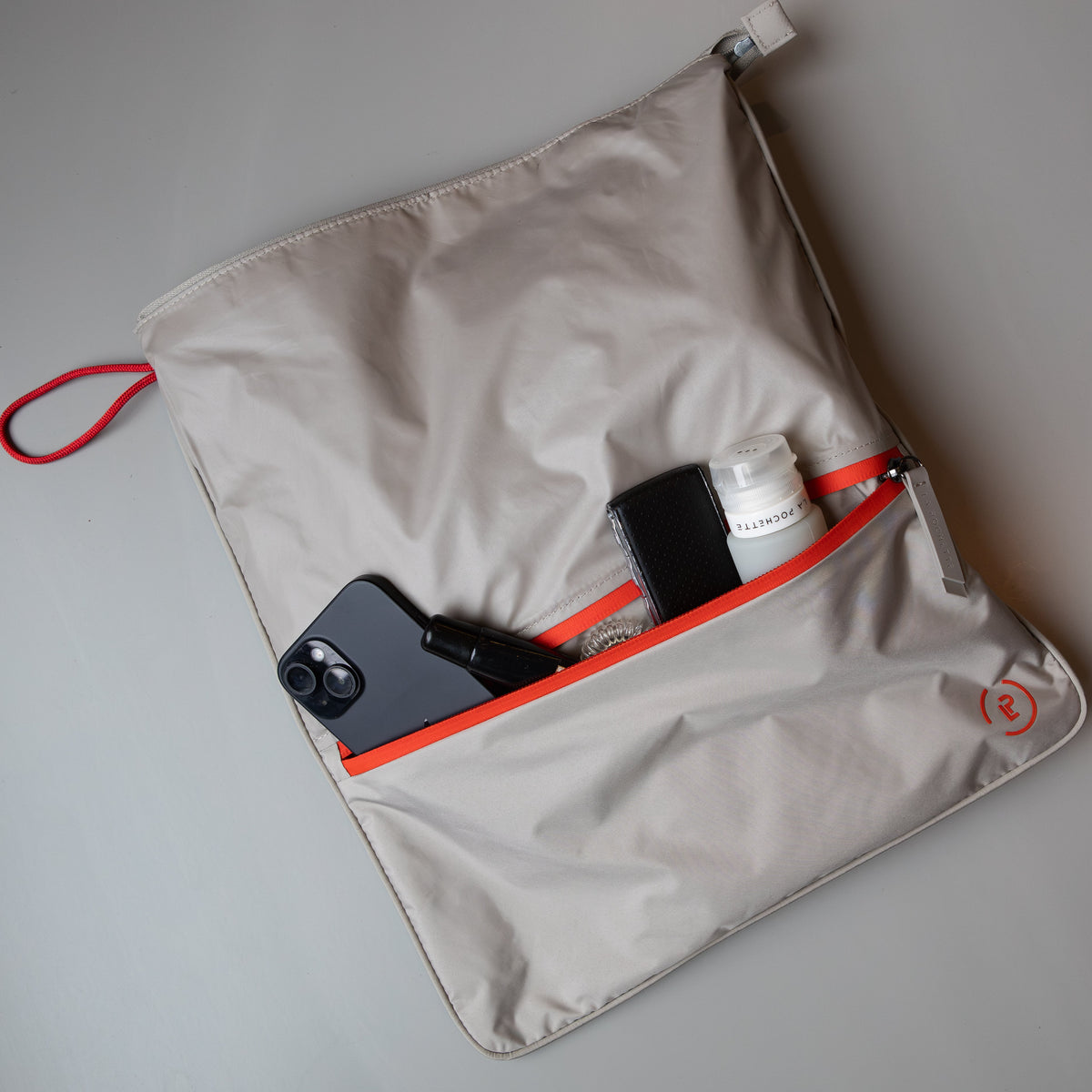 La Pochette antibacterial Sweat Bag in taupe and red with various everyday essentials shown in the front pocket