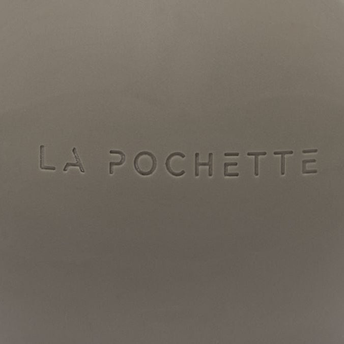 A matte taupe brown spherical massage ball with 'LA POCHETTE' embossed on the front, set against a clean white background with a soft shadow.