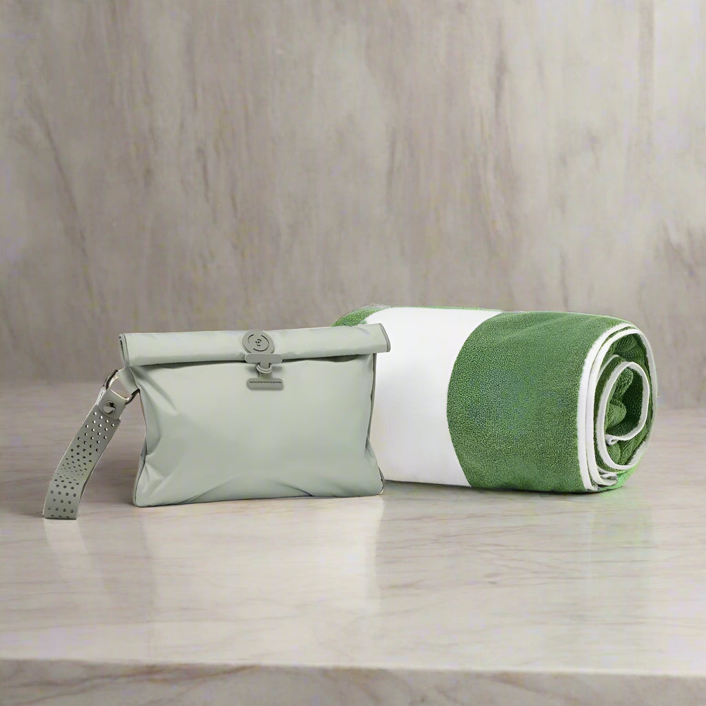 Green and white rolled-up towel with a green La Pochette Wet Bag on marble surface