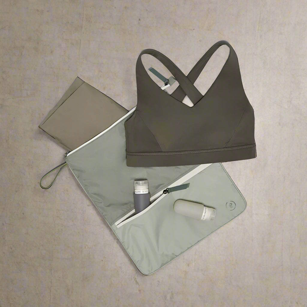 Green sports bra on a green La Pochette Sweat Bag with 2 silicone travel bottles on a grey background