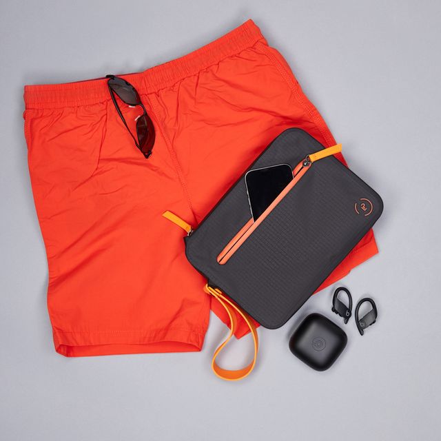Black waterproof Aqua Bag with orange details styled with orange swimming shorts, glasses and earphones, designed to keep wet and dry items separate