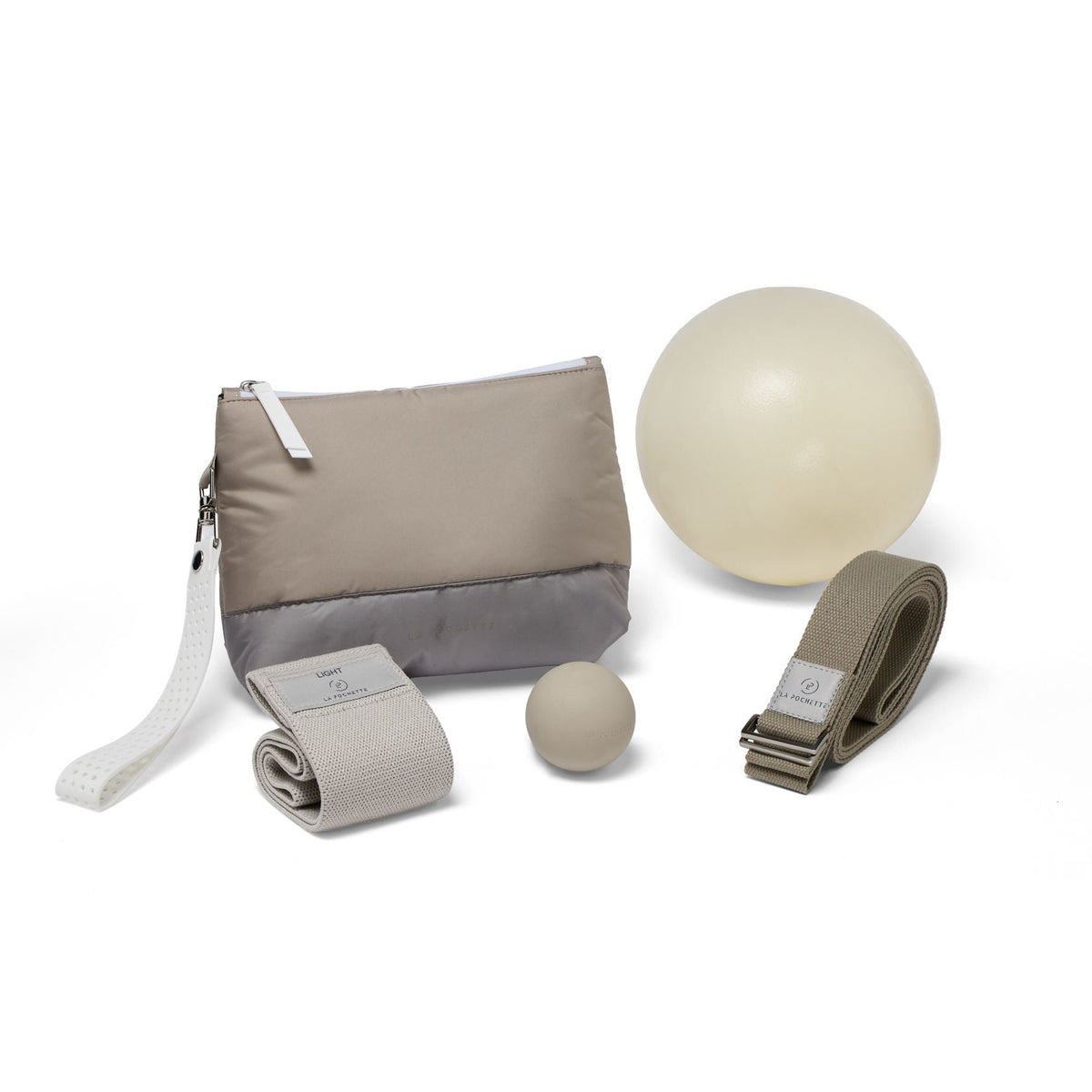 An assortment of workout accessories in beige and grey, including:
- an inflatable Pilates ball in ivory
- a grey yoga strap with a woven logo saying La Pochette
- a resistance band with a woven logo saying La Pochette
- a taupe small silicone recovery ball
- a La Pochette Everywhere pouch in grey and taupe with a white zip and a detachable silicone handle

On a white background 