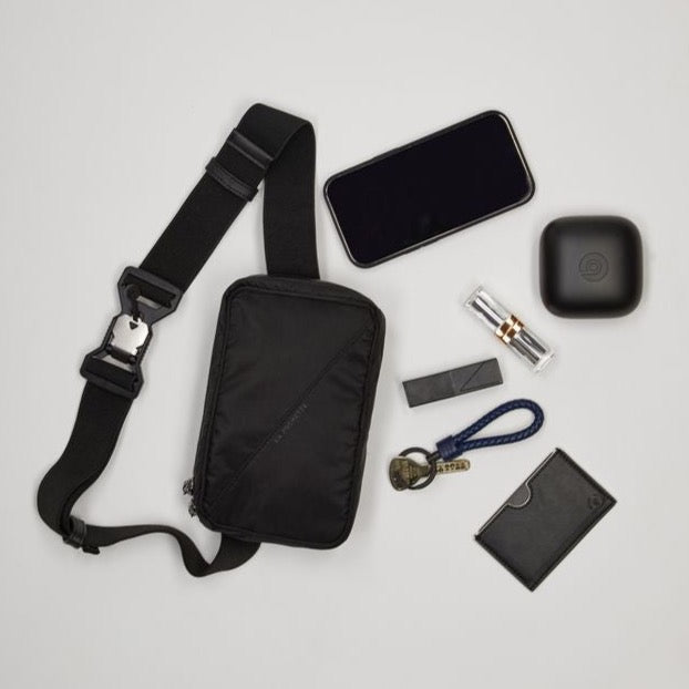 Belt bag in black showing various items such as a phone, lipstick and wallet lying next to it