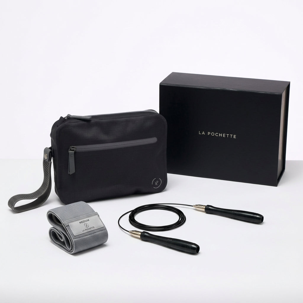 A black La Pochette waterproof aqua  bag with a grey zipper, shown with a black branded gift box, a grey resistance band and  and a black-and-silver skipping rope on a clean white background.