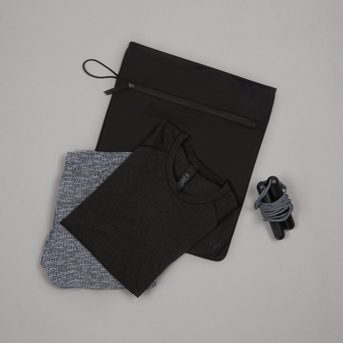 Black Kit Bag laid flat with folded gym clothes on top and the Tangram SmartRope laying beside it