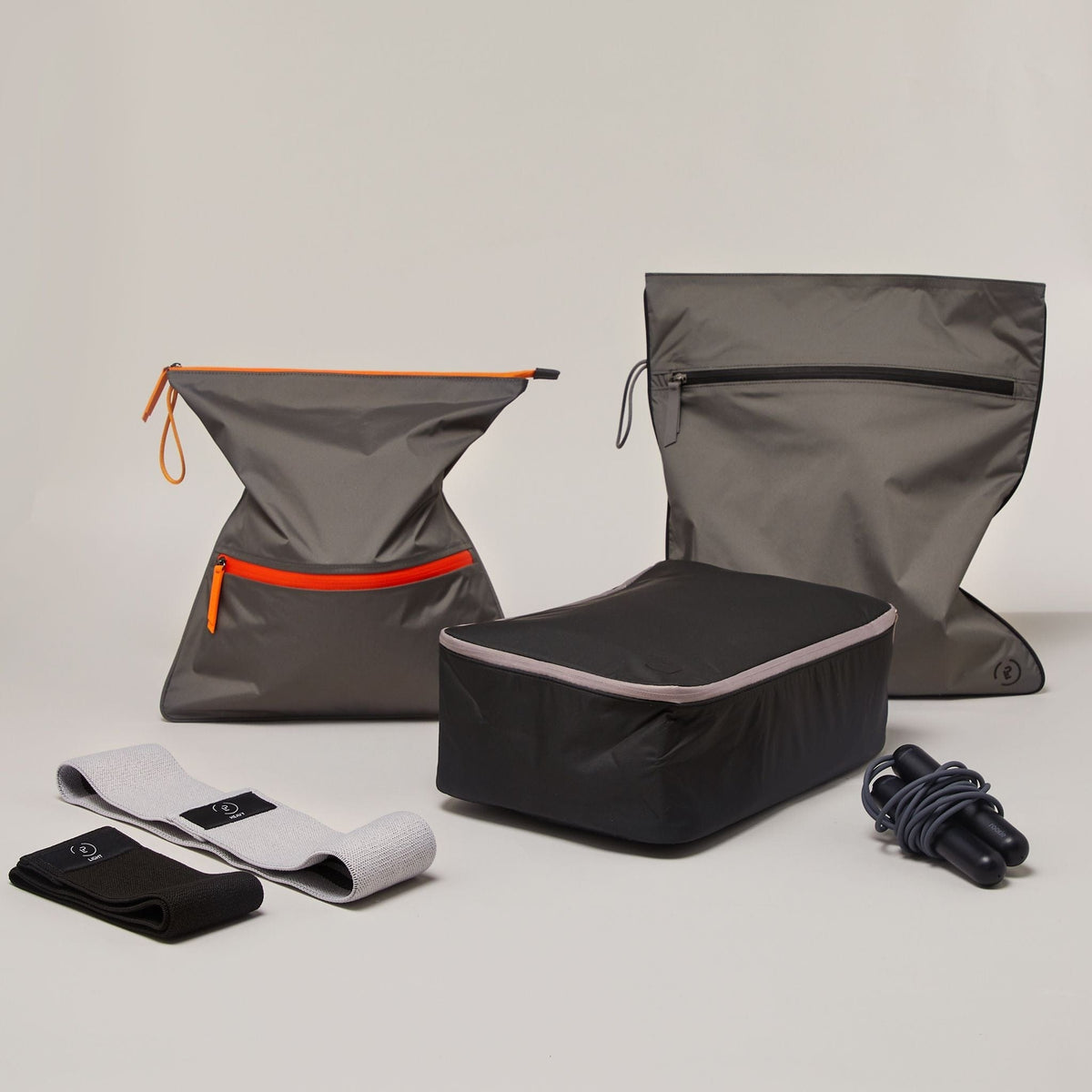 Kit Bag in dark grey with black trims next to a Sweat Bag with orange trims, a black Shoe Bag, resistance bands and the Tangram SmartRope