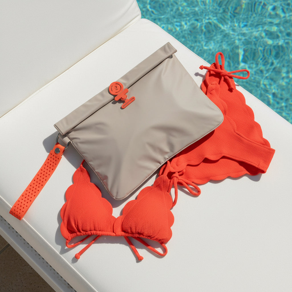 Red bikini set with waterproof la pochette beige wet bag with red detachable handle and clasp  on a white sunlounger by a pool