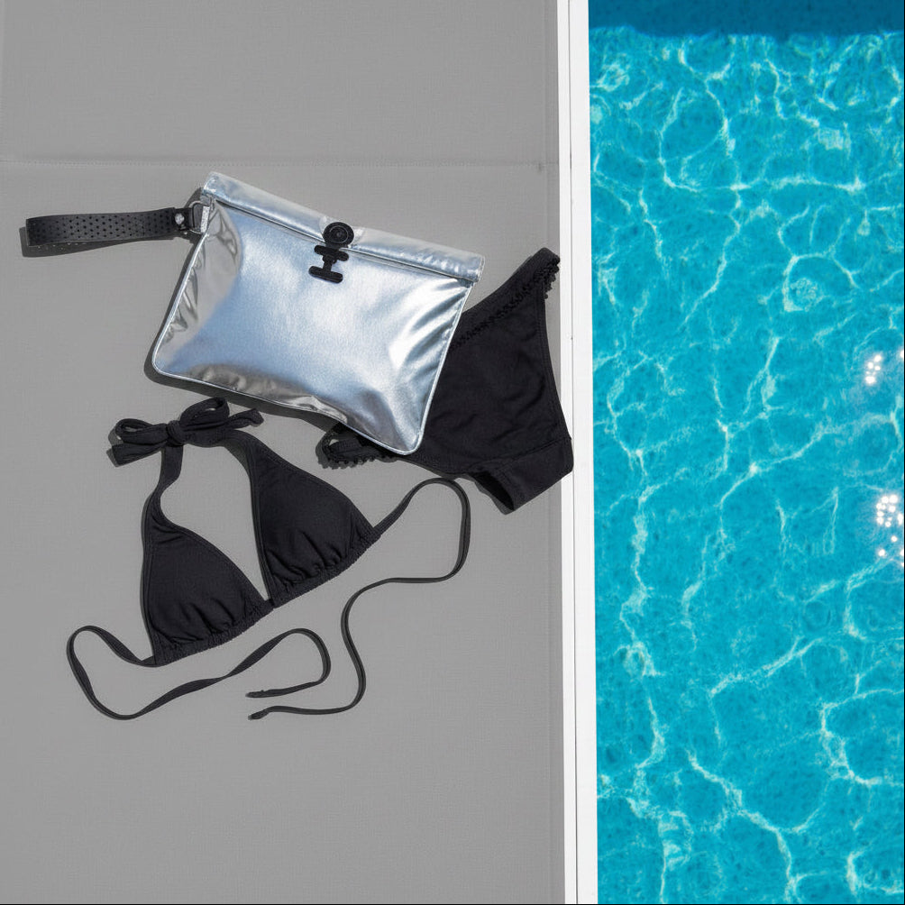 Black bikini set with silver la pochette waterproof wet bag on a sunlounger , next to a pool