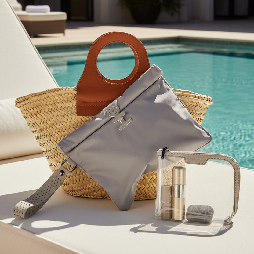 Dark taupe and soft  beige Large Wet Bag styled with a woven beach tote and small La Pochette clear pouch  on a sunlounger next to  pool