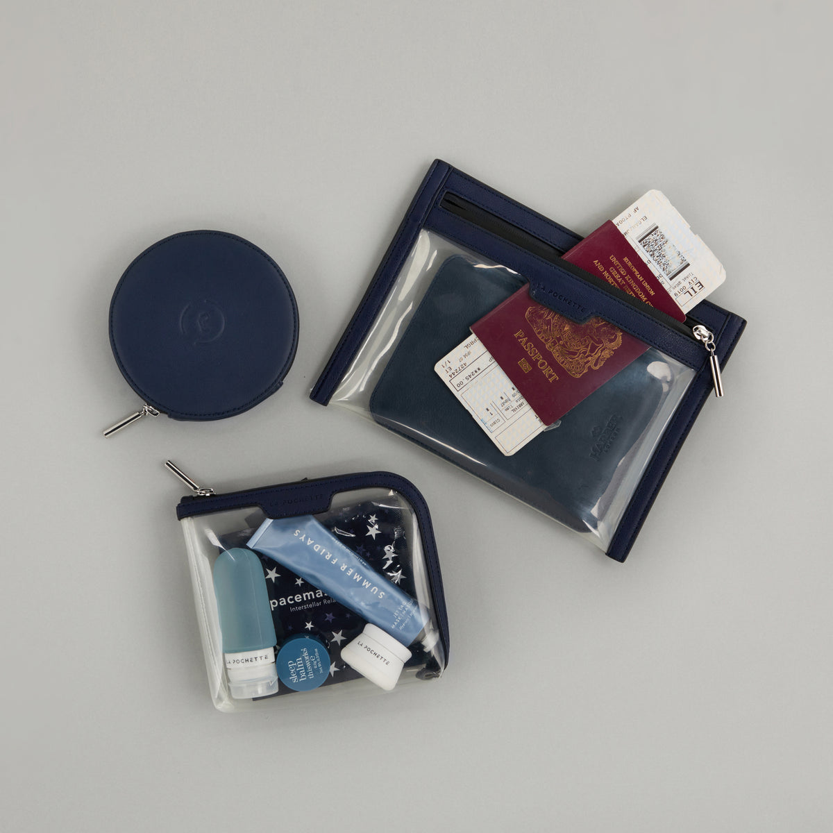 Anywhere Everywhere Wallet in Midnight Ink colourway containing a passport next to Small Anywhere Everywhere Pouch in Midnight Ink colourway holding La Pochette silicone travel bottles. Featured with Circle Purse in Midnight Ink