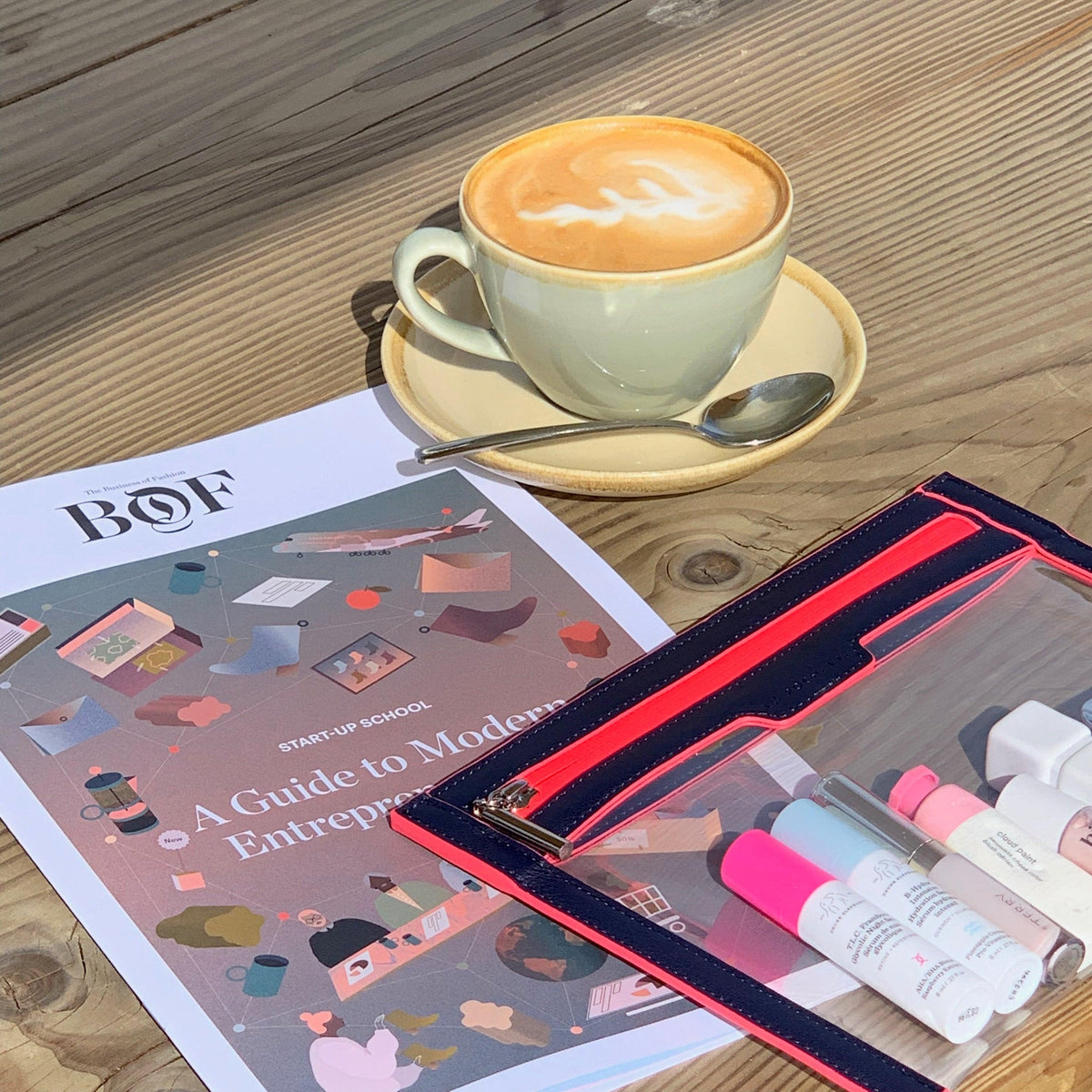 Anywhere Everywhere Wallet in Midnight Noen Pink colourway containing beauty accessories ontop of fashion magazine, next to a coffee