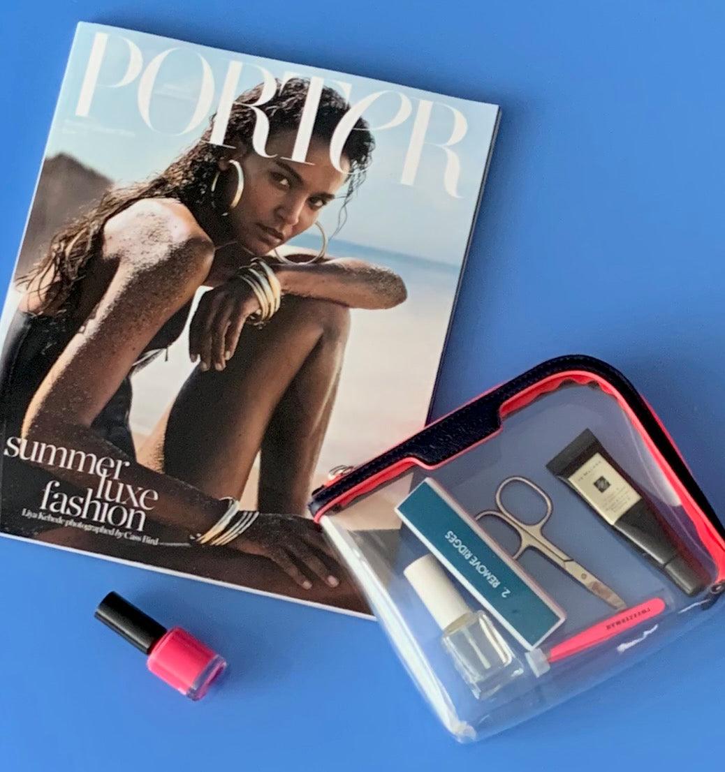 Small Anywhere Everywhere Pouch in Midnight Neon Pink colourway containing beauty accessories next to a fashion magazine 