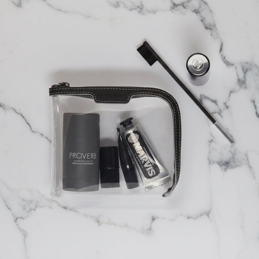 Small see through pouch with black and grey trims containing beauty accessories on  marble top
