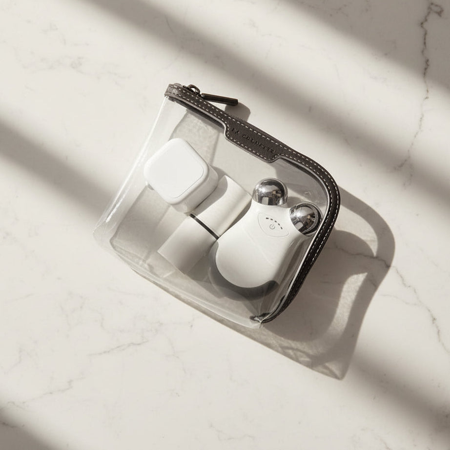 Small La Pochette clear pouch with black and grey trims containing electrical beauty accessories on a marble table top