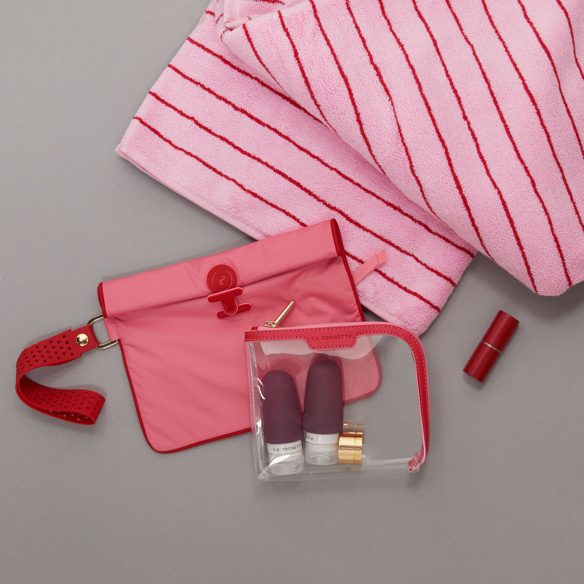 Small wet bag in Peony and Chilli colour way lying flat with a small Anywhere Everywhere Pouch containing La Pochette silicone travel bottles, a lipstick, and beach towel