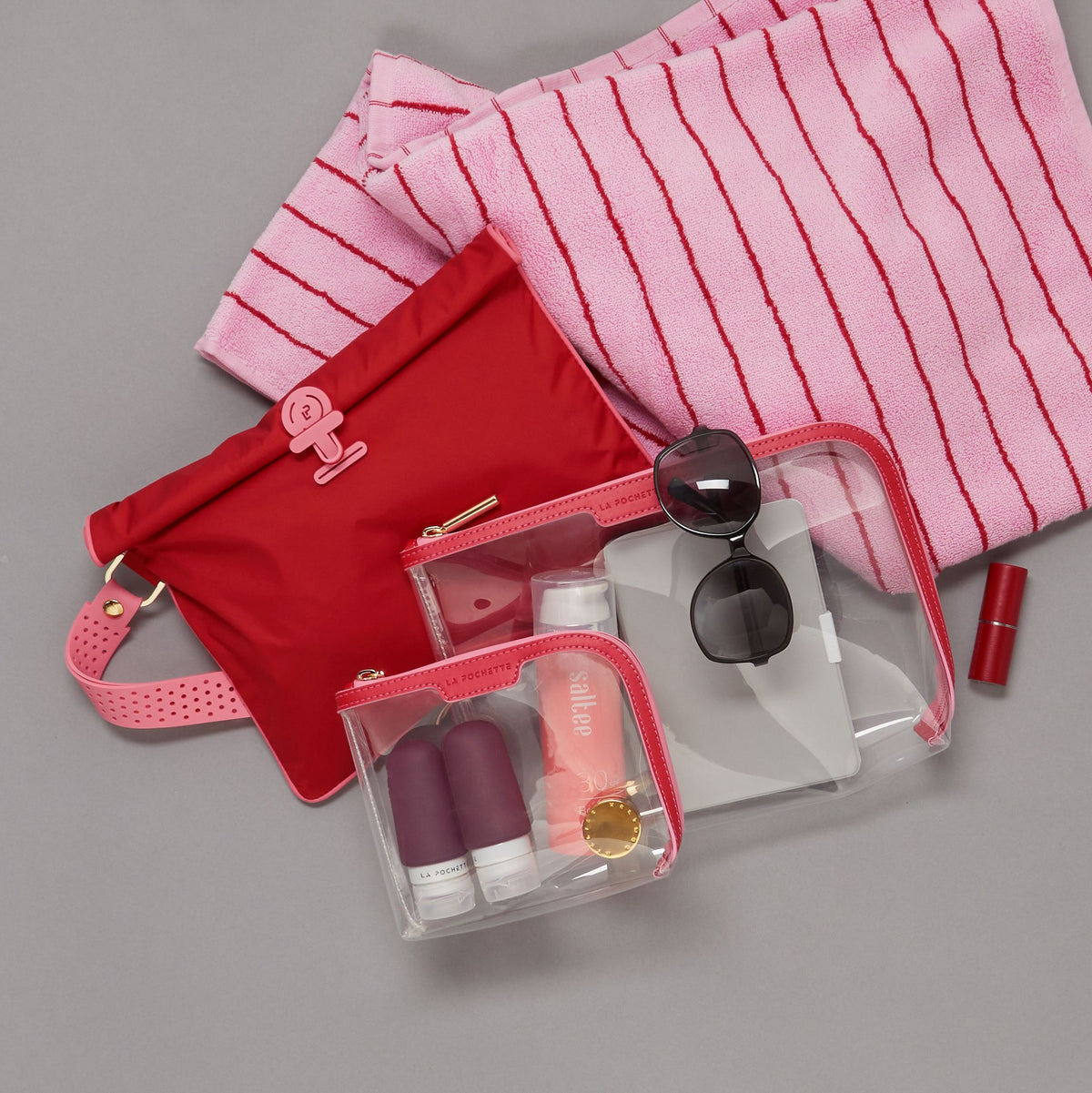 Large Wet Bag in Chilli and Peony colour way lying flat with a Large Anywhere Everything and Small Anywhere Everywhere Pouch containing La Pochette silicone travel bottles, a lipstick, and beach towel 