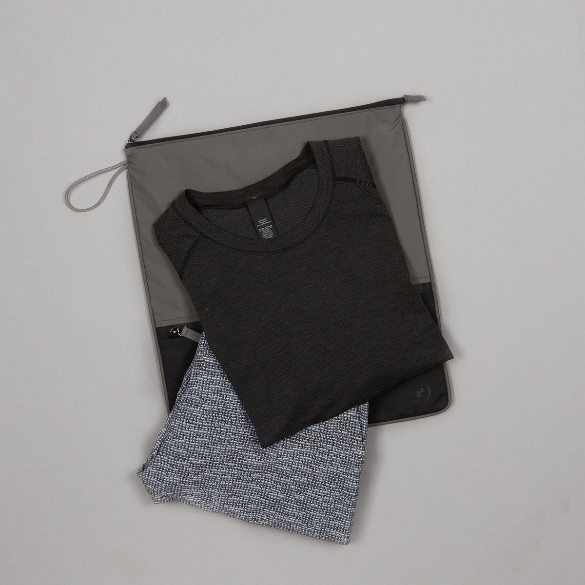 Two-tone grey and black Sweat Bag shown flat, with folded gym clothes layered on top.