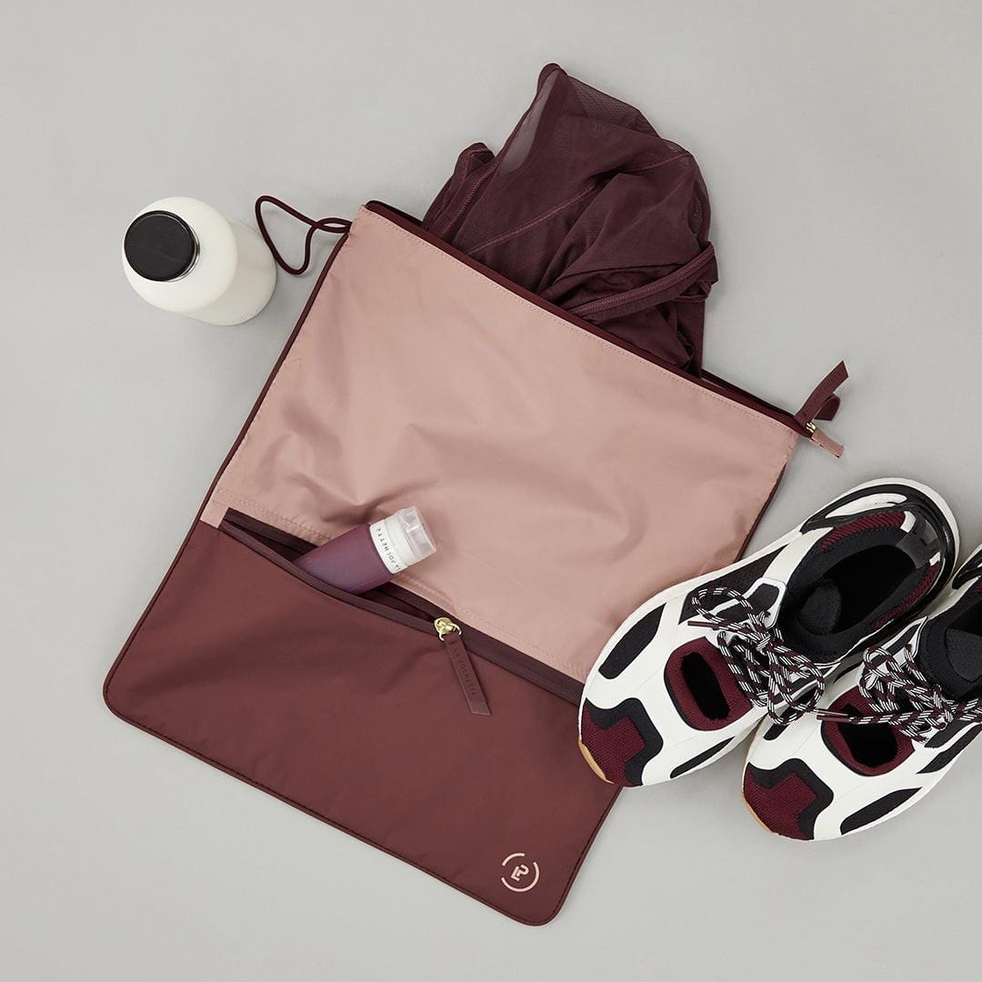 Soft pink and burgundy Sweat Bag shown flat, with gym clothes, trainers and La Pochette silicone travel bottle in the front pocket