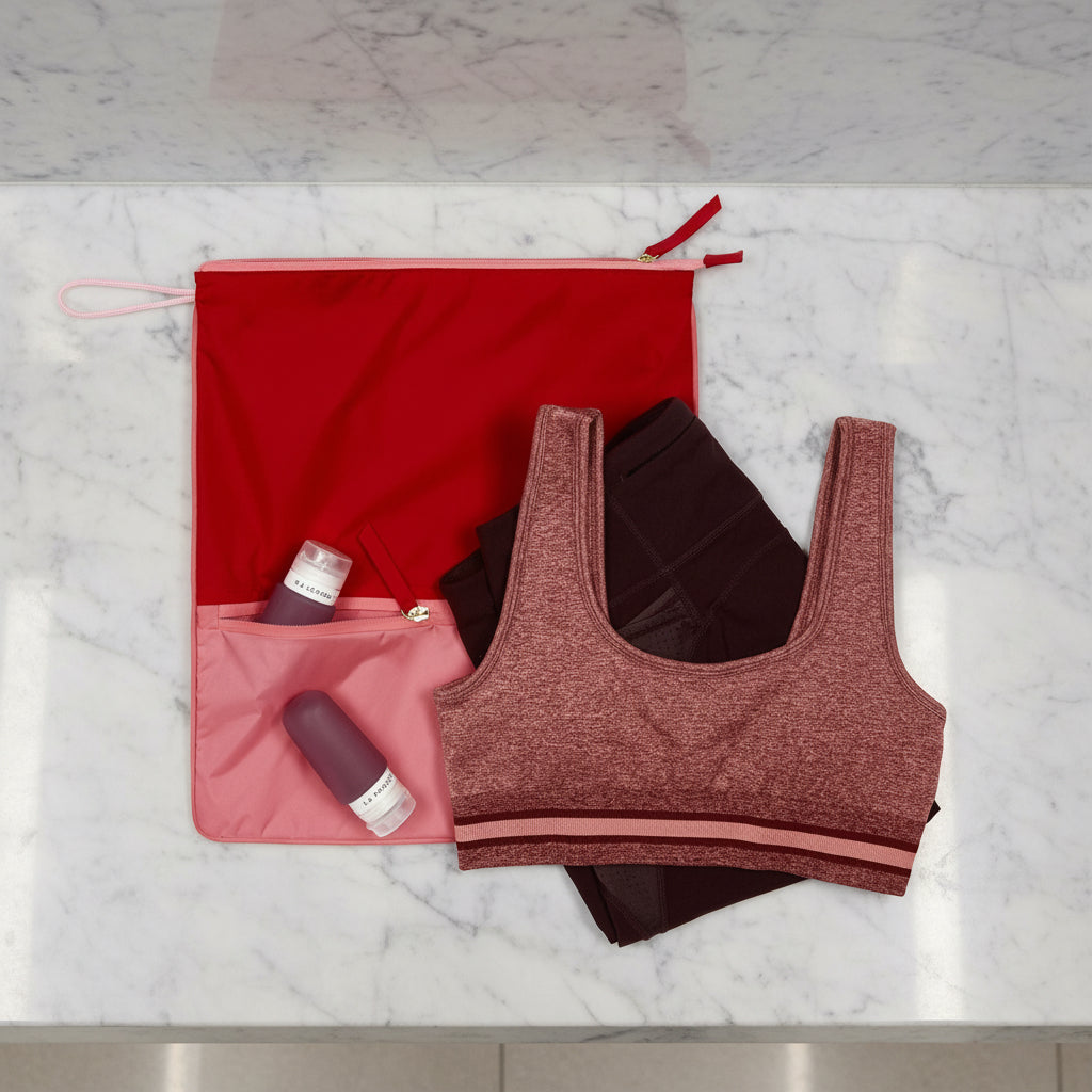 La Pochette antimicrobial Sweat Bag shown with gym kit, and post workout essentials, including the silicone travel bottles. On a light grey marble background.