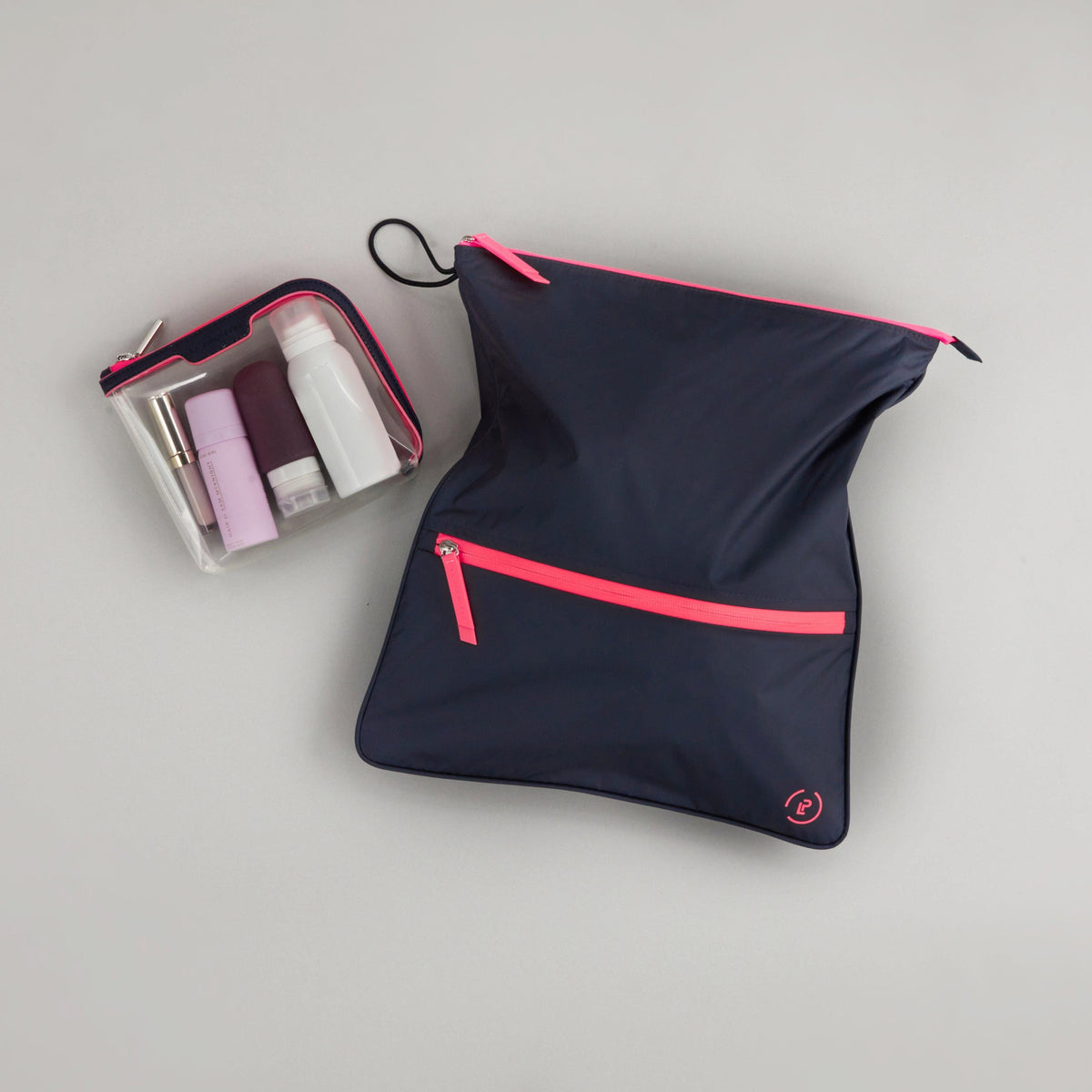 Midnight Neon Pink Sweat Bag laid flat, topped with a small La Pochette Anywhere Everything Bag holding La Pochette silicone travel bottles.